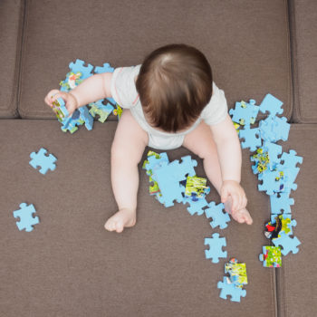 Baby boy playing with puzzle pieces on sofa in the living room at home
