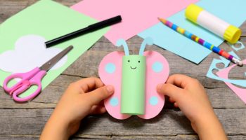 Small child holding paper butterfly in his hands. Child shows paper crafts. Funny butterfly made of colored paper. Office supplies on a wooden table. Children creativity concept
