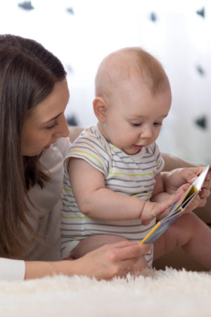 Mother showing images in a book to her cute baby son at home