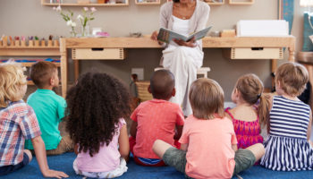 Teacher At Montessori School Reading To Children At Story Time