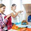 Portrait of smiling young mother with teenage daughter folding clothes after laundry